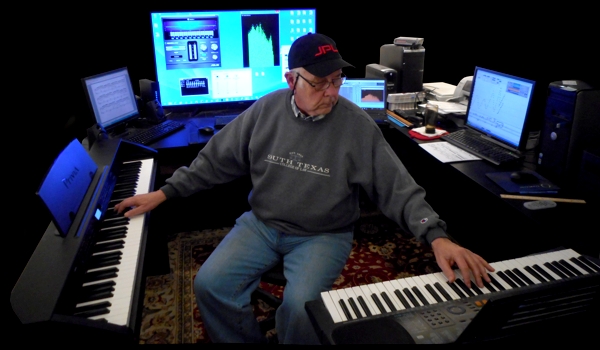 Photo of Reeves Motal laying down music tracks in his studio using two keyboards and four computers all networked together.  The photo was taken in the winter time, hence the South Texas School of Law sweatshirt and the JPL (Jet Propulsion Lab at Cal-Tech) baseball cap.